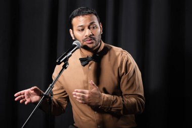 indian comedian performing stand up comedy and telling jokes in microphone on black stage clipart