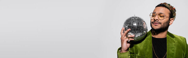 eastern hip hop performer in green velvet blazer and crown holding disco ball isolated on grey, banner