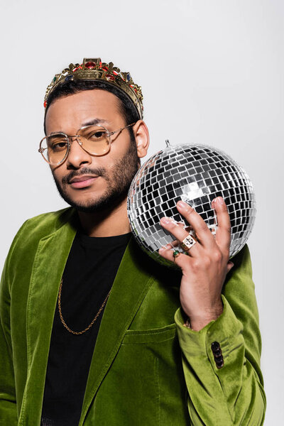indian hip hop performer in green velvet blazer and crown holding disco ball isolated on grey