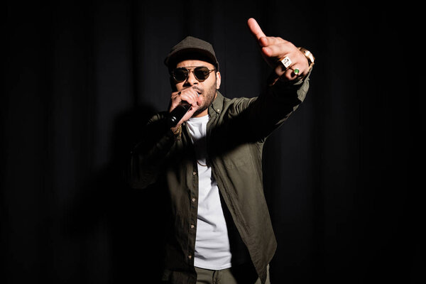 indian hip hop performer in sunglasses singing in microphone on black