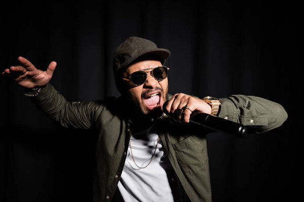 eastern hip hop singer in sunglasses singing in microphone on black