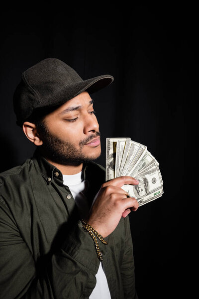 indian hip hop singer in cap holding dollar banknotes isolated on black 