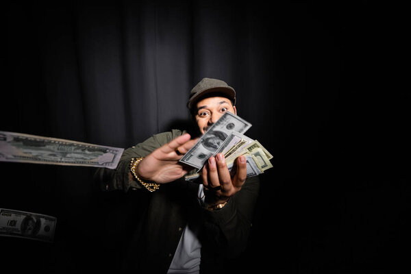 rich indian hip hop performer throwing dollar banknotes on black 