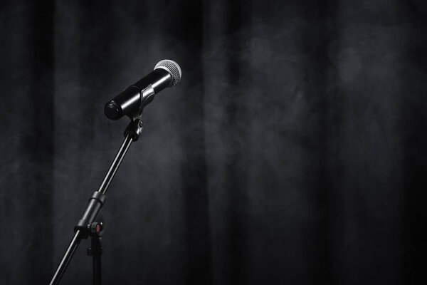 микрофон стоит на черной сцене с занавесом и дымом
