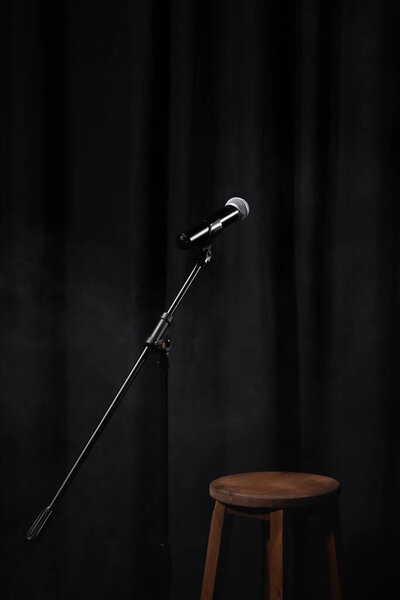 микрофон на стенде на черной сцене с занавесом и деревянным стулом