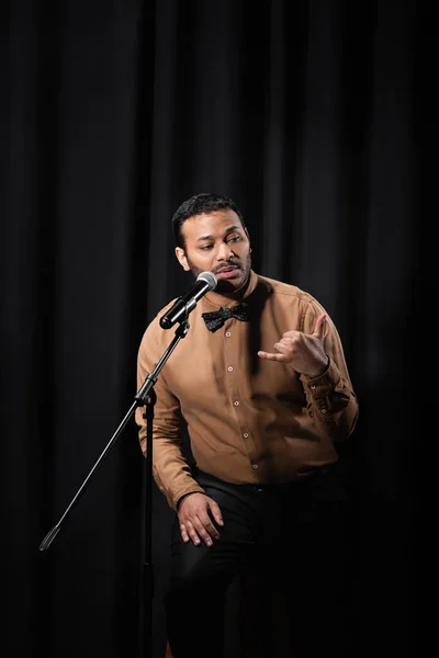 indian comedian performing stand up comedy and telling jokes in microphone on black