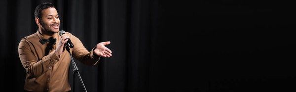 индийский комик выступает стенд-ап комедия и рассказывает шутки в микрофоне, жестикулируя на черный, баннер