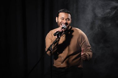 Mutlu Hintli komedyen sandalyeye oturup stand-up komedisi yapıyor.