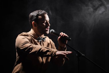 Hintli komedyen komedi gösterisi yapıyor. Mikrofona stand-up komedisi yapıyor. Siyaha dumanla bakıyor.