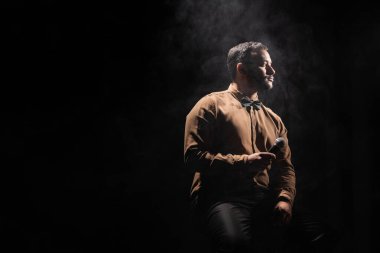 Hintli komedyen mikrofonu tutuyor ve siyaha dumanla bakıyor.