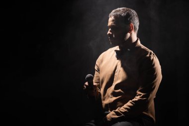 indian stand up comedian holding microphone and looking away on black with smoke