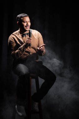 Hintli komedyen oturur ve sahnede stand up komedisi yapar. Siyahta dumanla mikrofona geçer. 