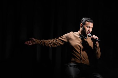 Doğulu komedyen oturuyor ve şarkı söylüyor stand-up komedisini mikrofona yerleştiriyor. 