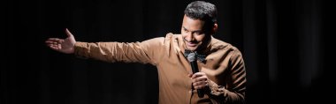 Gülümseyen Hintli komedyen stand up komedisini siyah pankartta mikrofona yerleştiriyor.