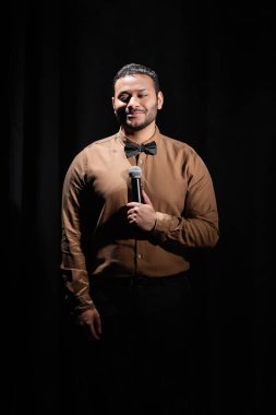 Gülümseyen Orta Doğu komedyeni stand up komedisini siyah üzerine mikrofona yerleştiriyor. 