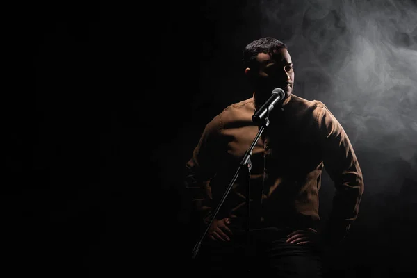 indian comedian sitting on chair and performing stand up comedy into microphone on black with smoke