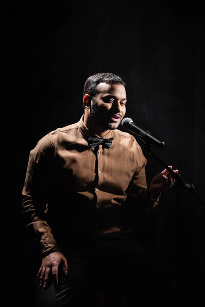indian stand up comedian telling jokes into microphone on dark stage isolated on black 