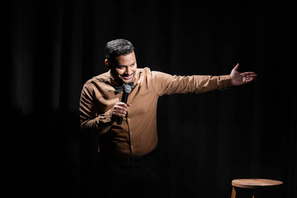 smiling indian comedian performing stand up comedy into microphone on black 