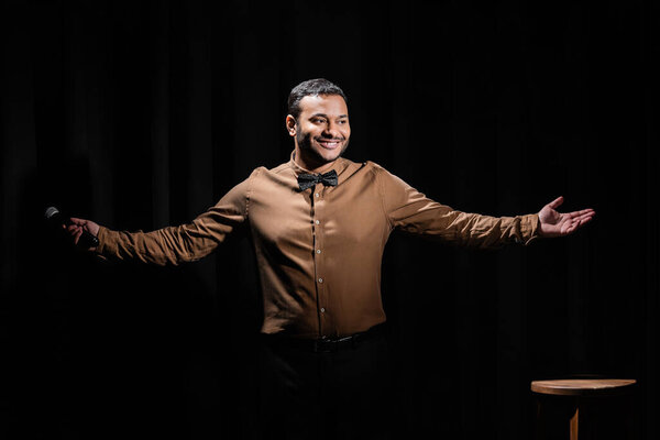 happy middle east comedian gesturing and holding microphone on black 