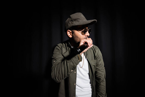 middle east hip hop singer in cap and sunglasses singing into microphone on black 