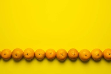 Flat lay with tangerines in line on yellow background with copy space