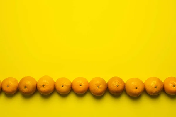 Flat lay with tangerines in line on yellow background with copy space