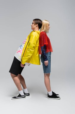 Side view of trendy couple standing back to back on grey background