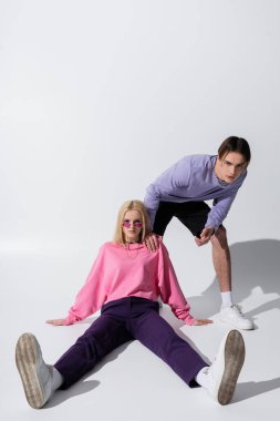 Pembe güneş gözlüklü sarışın kadın, gri arka planda erkek arkadaşının yanında oturuyor.