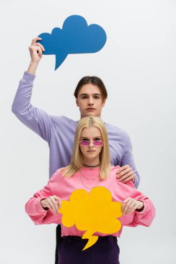 Stylish couple holding thought bubbles and looking at camera isolated on grey 