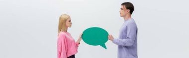 Side view of man and woman in sweatshirts holding speech bubble isolated on grey, banner 