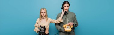 Trendy young woman holding handset near boyfriend isolated on blue, banner 