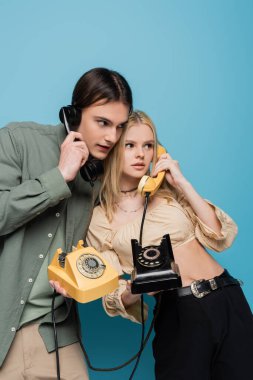 Fashionable couple talking on retro telephones on blue background 