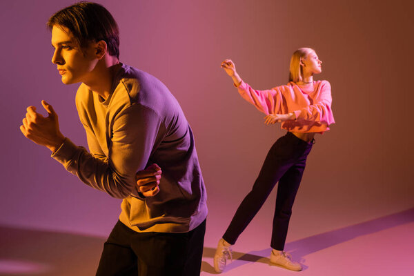 Вид сбоку на молодую пару в толстовках на фиолетовом фоне с освещением и тенью 