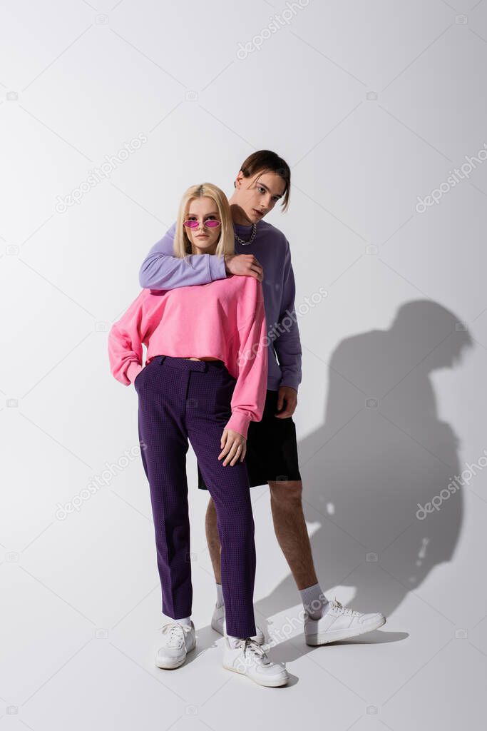 Stylish man hugging girlfriend in sunglasses on grey background