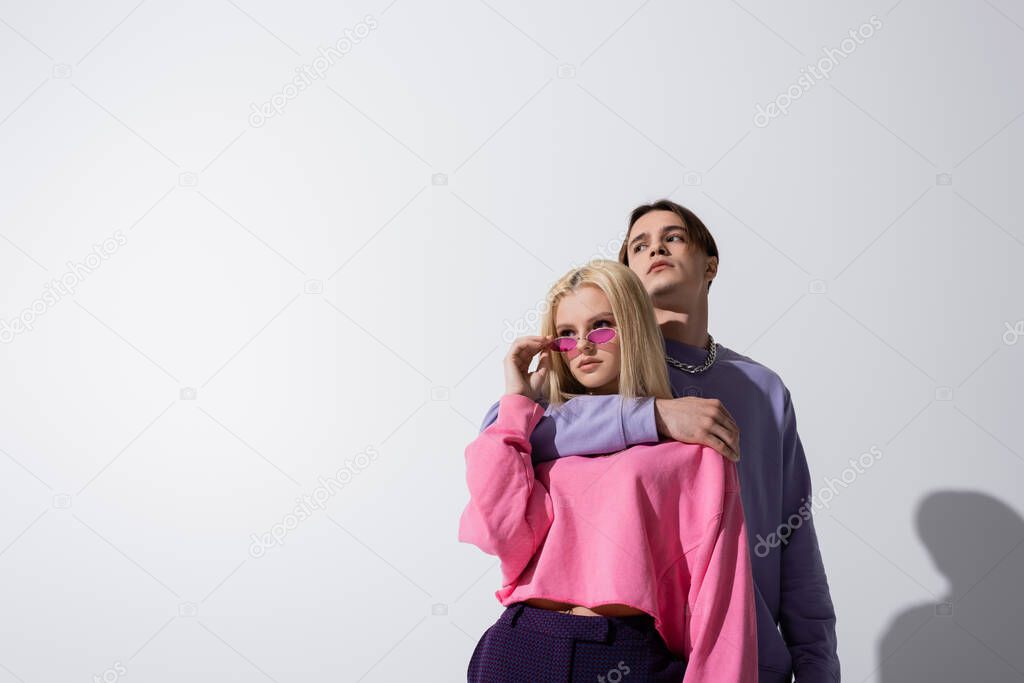 Man in purple sweatshirt embracing girlfriend in sunglasses on grey background