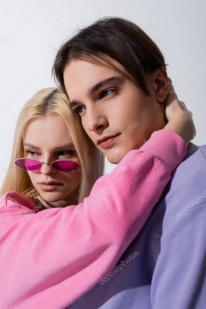 Young blonde woman in sunglasses hugging boyfriend isolated on grey 