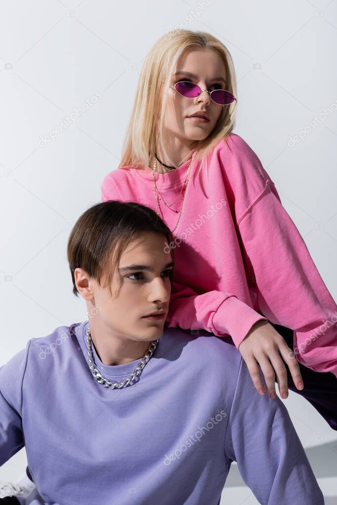 Stylish couple in sweatshirts looking away on grey background