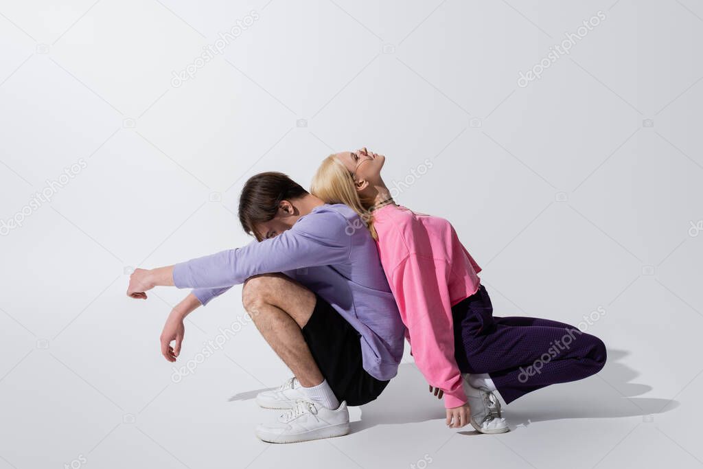 Side view of couple in sweatshirts posing back to back on grey background