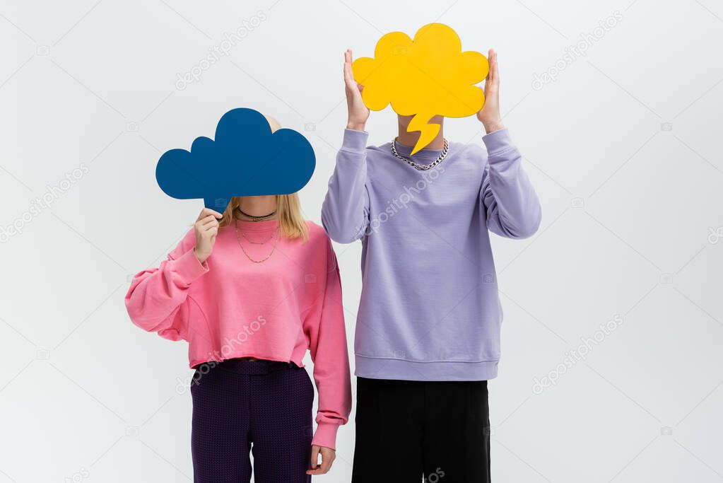 Young couple holding thought bubbles near faces isolated on grey 