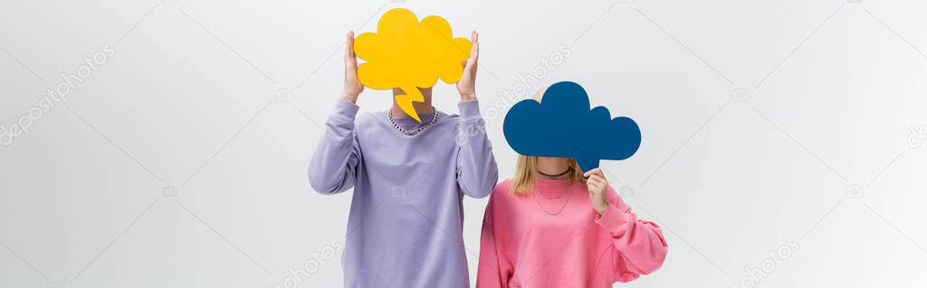 Young couple holding thought bubbles near faces isolated on grey, banner 