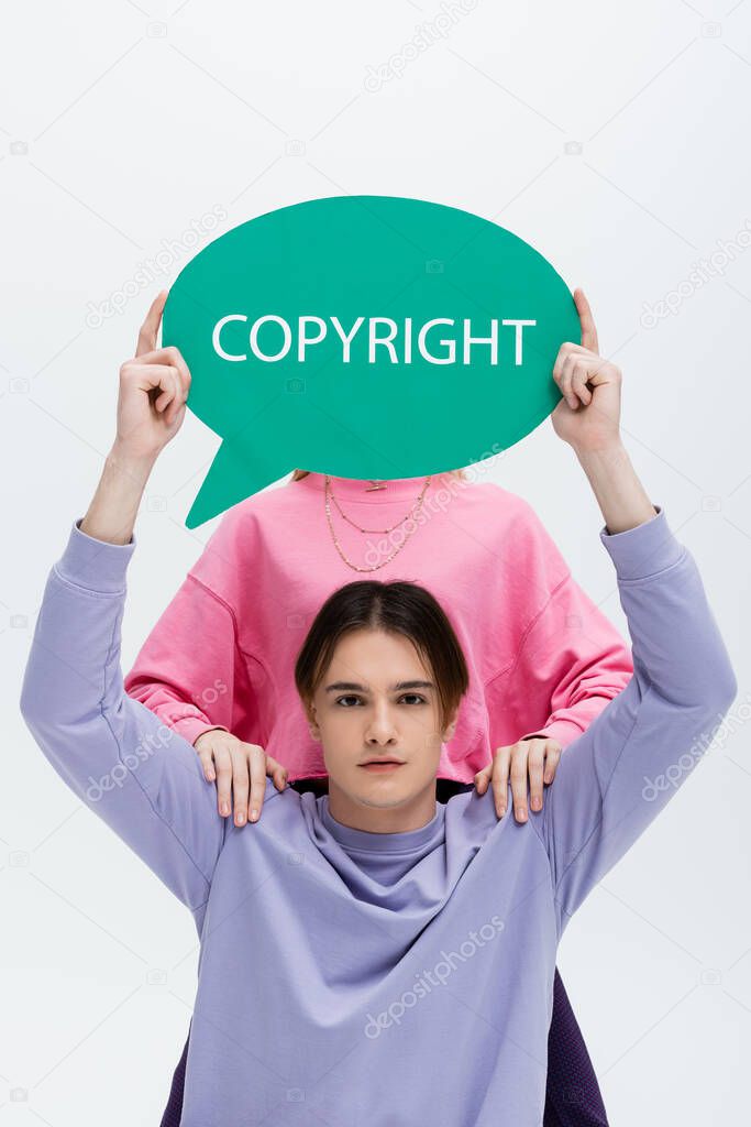 Man in sweatshirt holding speech bubble with copyright lettering near girlfriend isolated on grey 