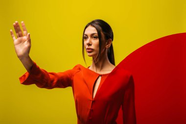 stylish young woman in red dress showing stop sign near round shape glass isolated on green 