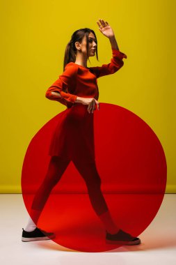 full length of stylish young woman in red dress holding round shape glass and gesturing on green 