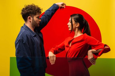 side view of trendy couple holding different shapes glass while posing isolated on yellow