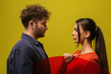 side view of trendy and young models posing near round shape glass isolated on green