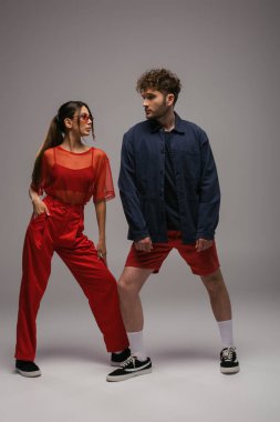 Moda kıyafetleri ve güneş gözlükleriyle gri renkte poz veren şık modeller.