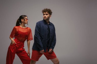 stylish models in trendy outfits and sunglasses posing isolated on grey