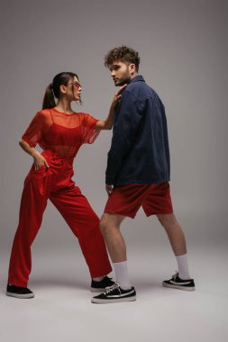 Moda kıyafetli ve güneş gözlüklü şık bir kadın. Gri elbiseli bir adamın yanında poz veriyor.