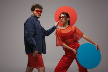 Mavi ve kırmızı elbiseli genç bir çift gri kutuda yuvarlak şekilli kutular tutuyorlar.