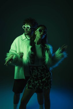 Güneş gözlüklü modaya uygun genç modeller koyu mavi üzerinde poz veriyorlar.